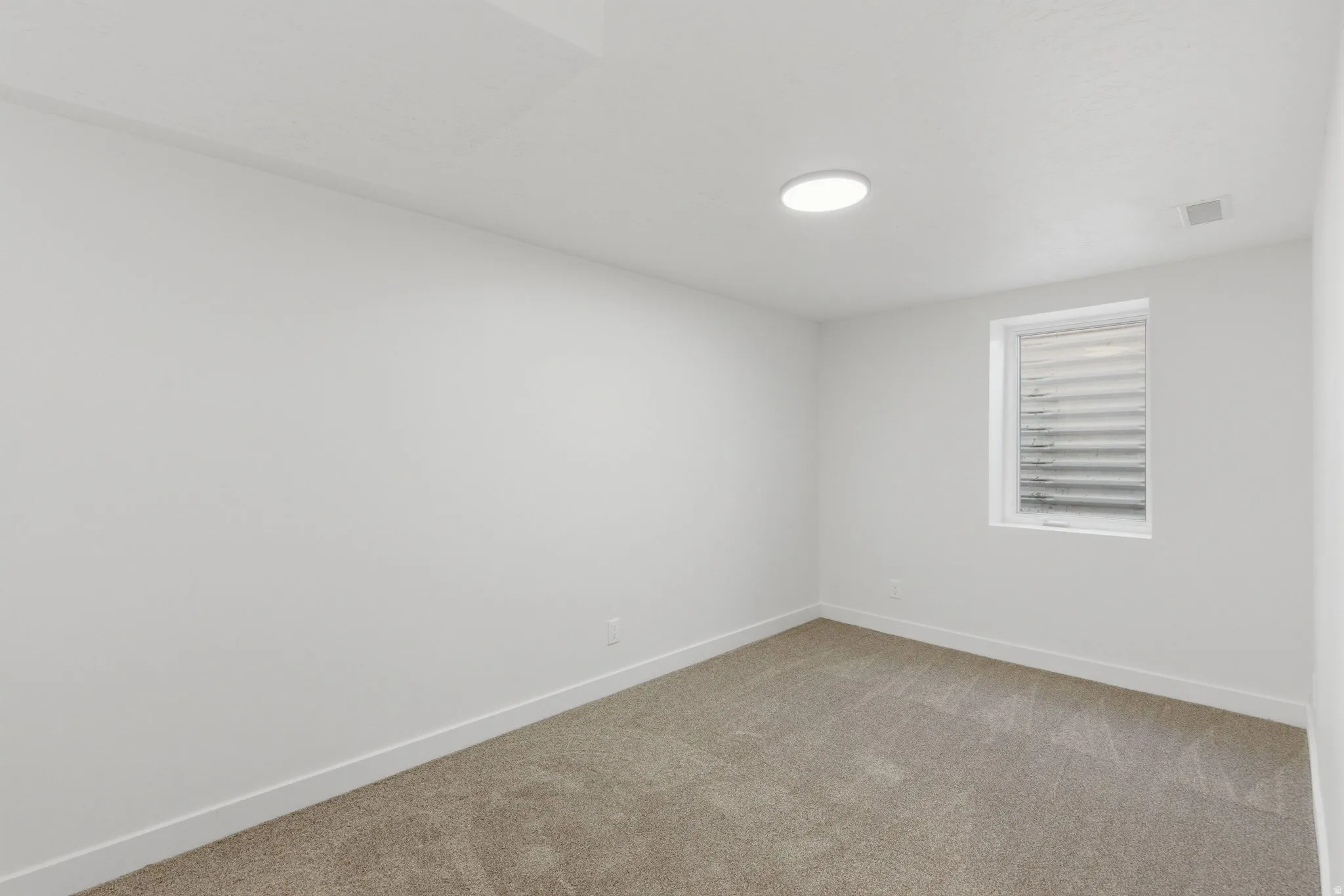 Light-filled room featuring neutral-toned carpeting, white walls, and a contemporary ceiling light fixture