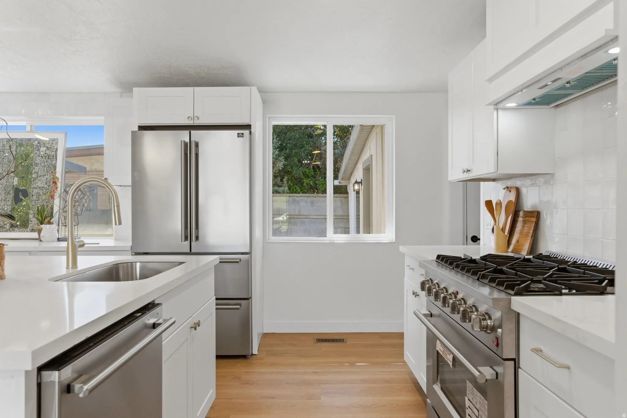Modern kitchen featuring white cabinetry, light-toned countertops, stainless steel appliances, and wood-finish flooring