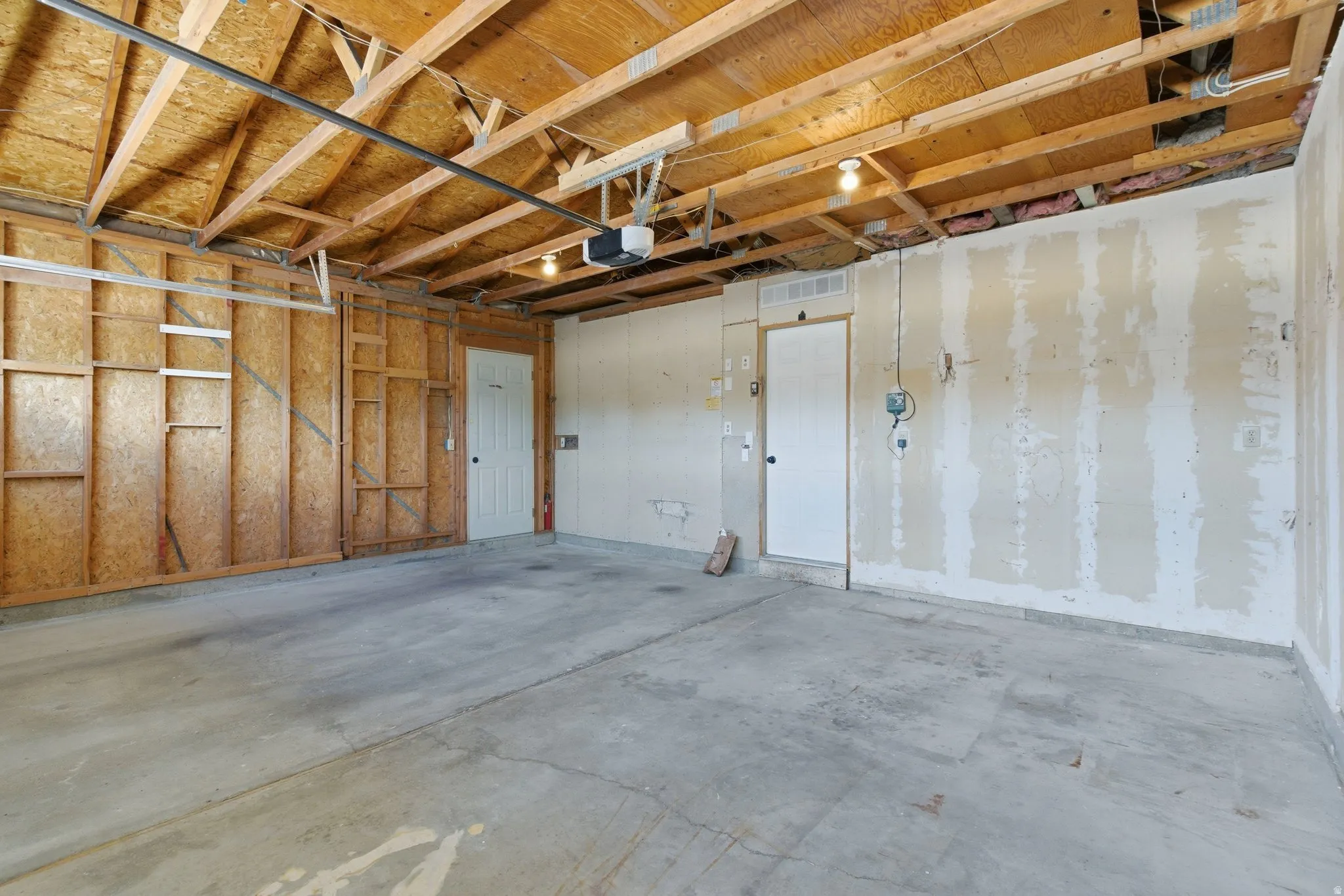 Spacious two-car garage featuring a concrete floor, exposed wood ceiling joists, and two interior access doors