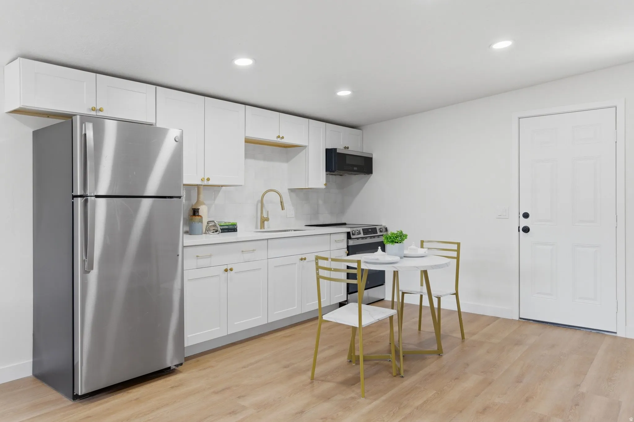 Sleek kitchen featuring white cabinetry, stainless steel appliances, wood-finish flooring, recessed lighting, and a paneled entry door
