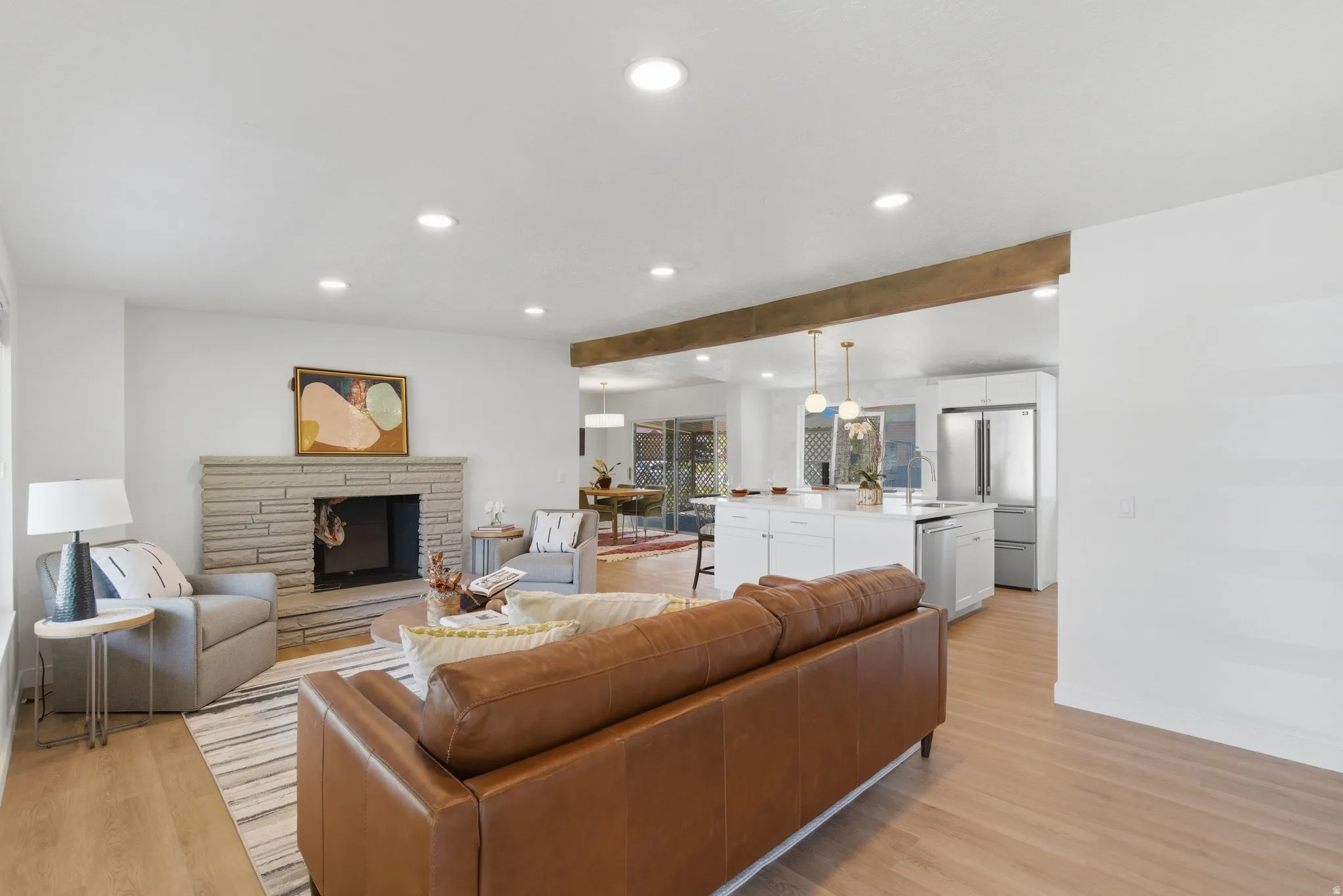 Spacious living area featuring light wood-finish flooring, recessed lighting, and a stacked stone fireplace
