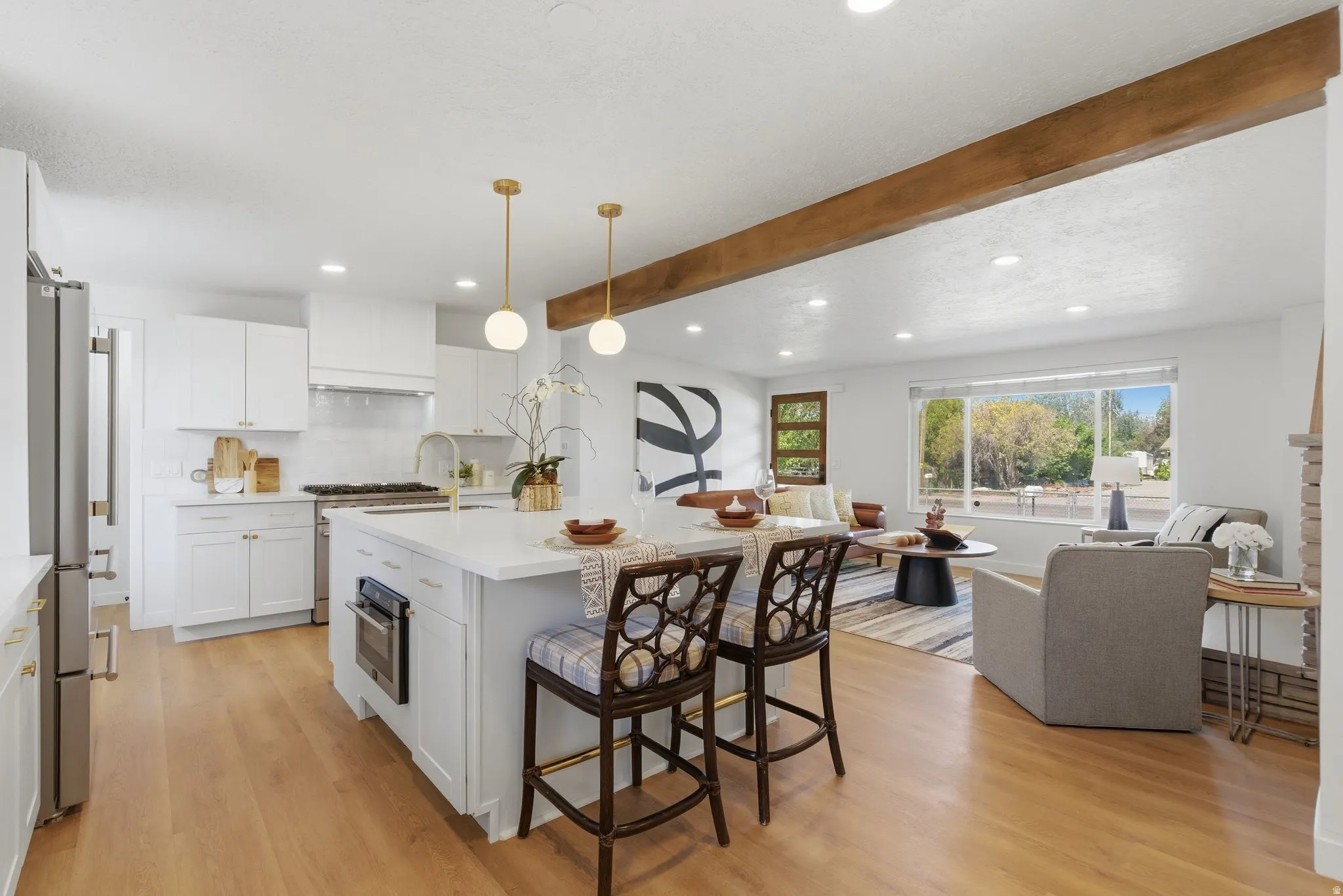Open-concept living space featuring a central kitchen island with seating, a large picture window, wood-finish flooring, recessed lighting, and an exposed ceiling beam