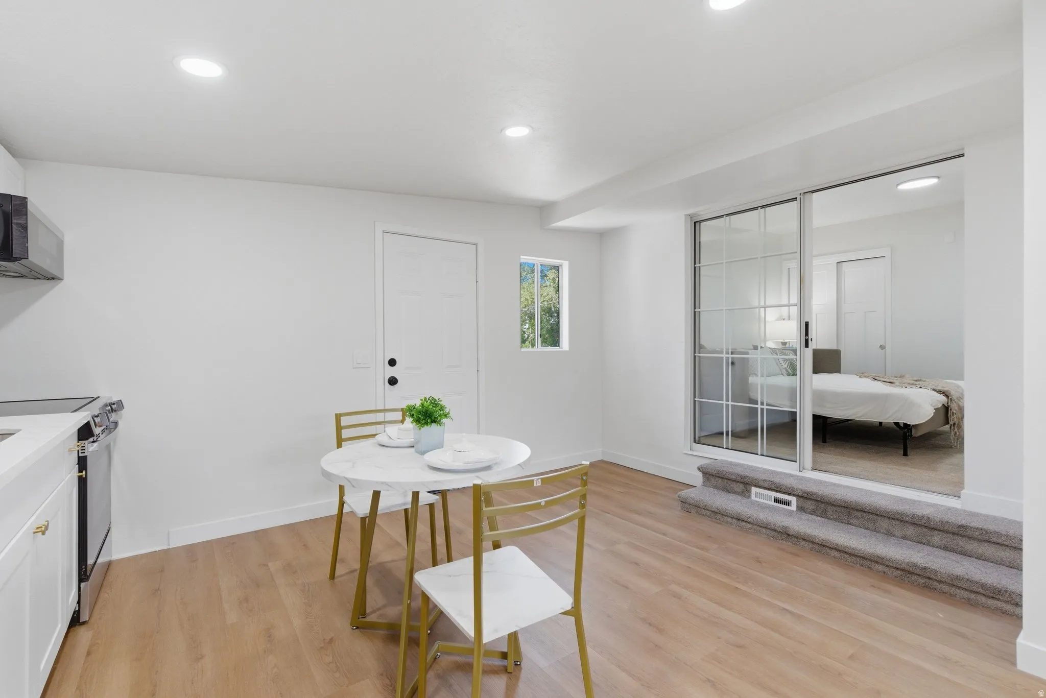 Open-concept living space with wood-finish flooring, recessed lighting, and a white kitchen featuring a stainless steel range and microwave
