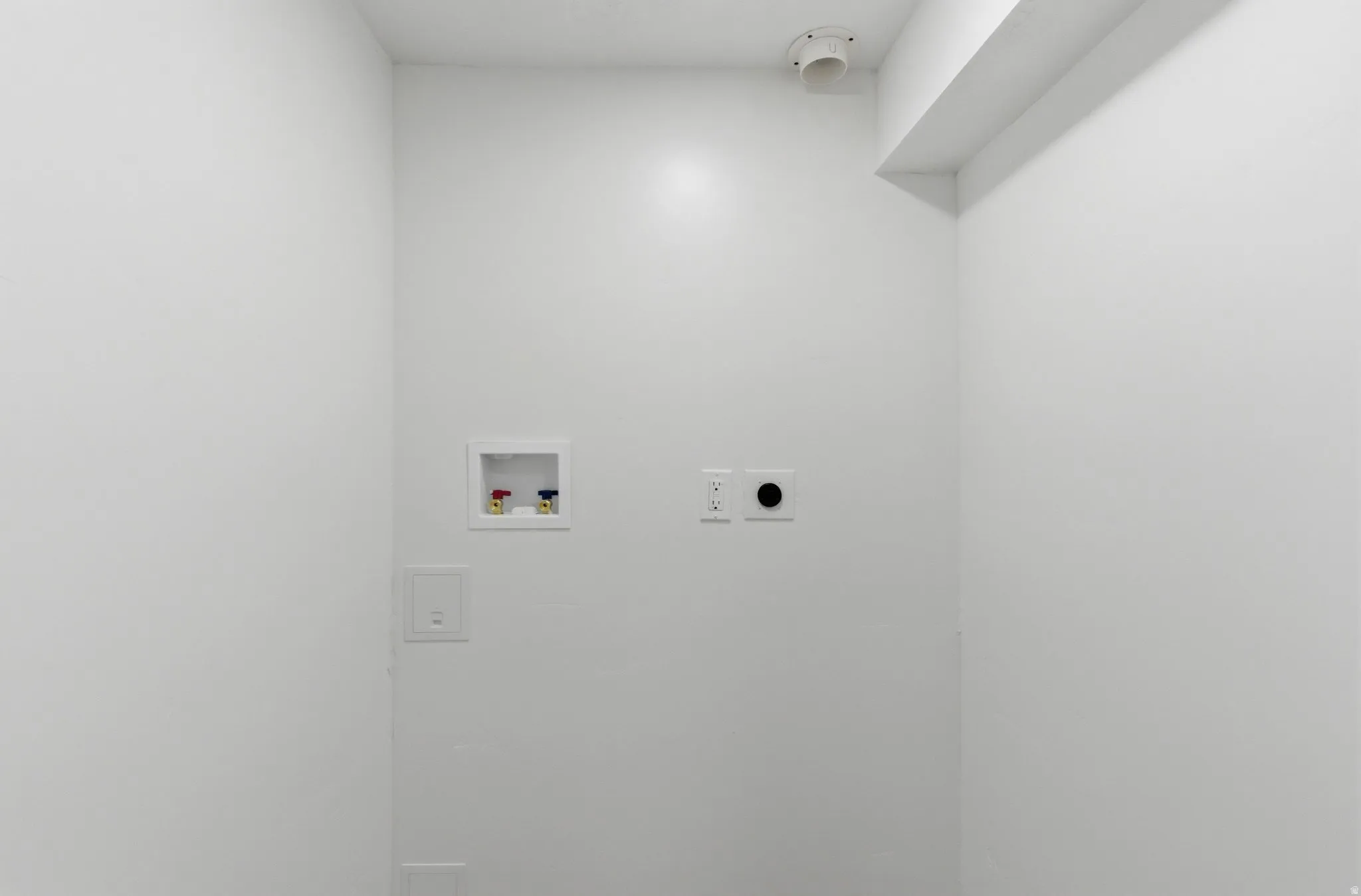 Utility area with white painted walls, featuring a water hookup box, electrical outlets, and a dryer vent