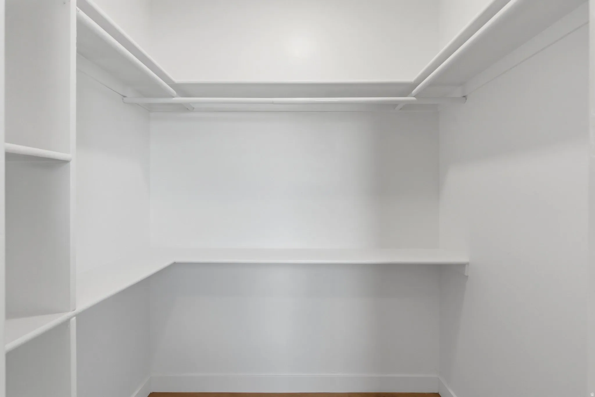 Walk-in closet featuring white built-in shelving, hanging rods, and wood-finish flooring