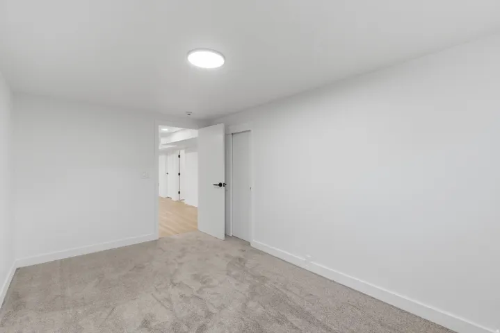 Carpeted room featuring a white door with black hardware, white baseboards, and a circular flush-mount ceiling light