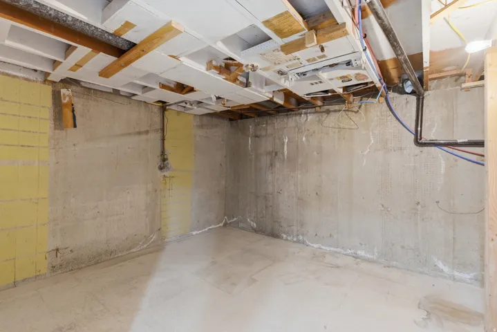Unfinished basement featuring exposed concrete walls and flooring, open ceiling joists, and visible utility lines