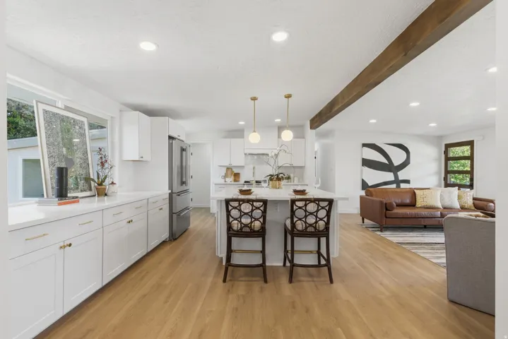 Open-concept kitchen featuring an island with pendant lighting, white cabinetry, integrated stainless steel appliances, and wood-finish flooring throughout