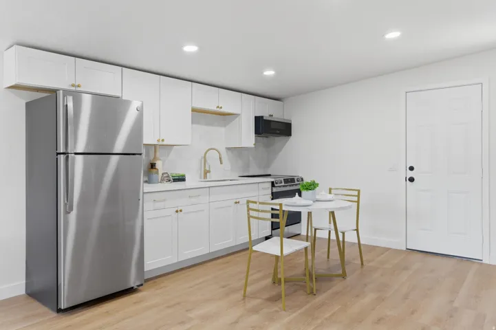 Sleek kitchen featuring white cabinetry, stainless steel appliances, wood-finish flooring, recessed lighting, and a paneled entry door
