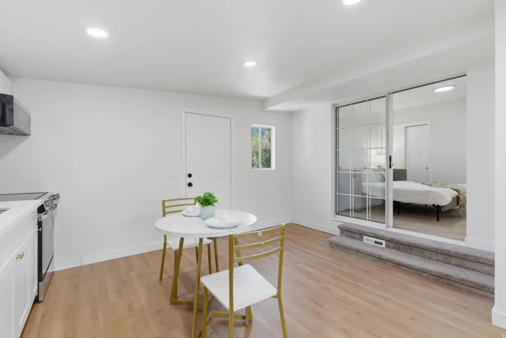 Open-concept living space with wood-finish flooring, recessed lighting, and a white kitchen featuring a stainless steel range and microwave