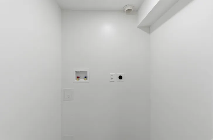 Utility area with white painted walls, featuring a water hookup box, electrical outlets, and a dryer vent