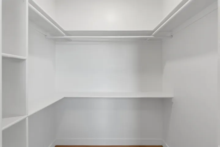 Walk-in closet featuring white built-in shelving, hanging rods, and wood-finish flooring