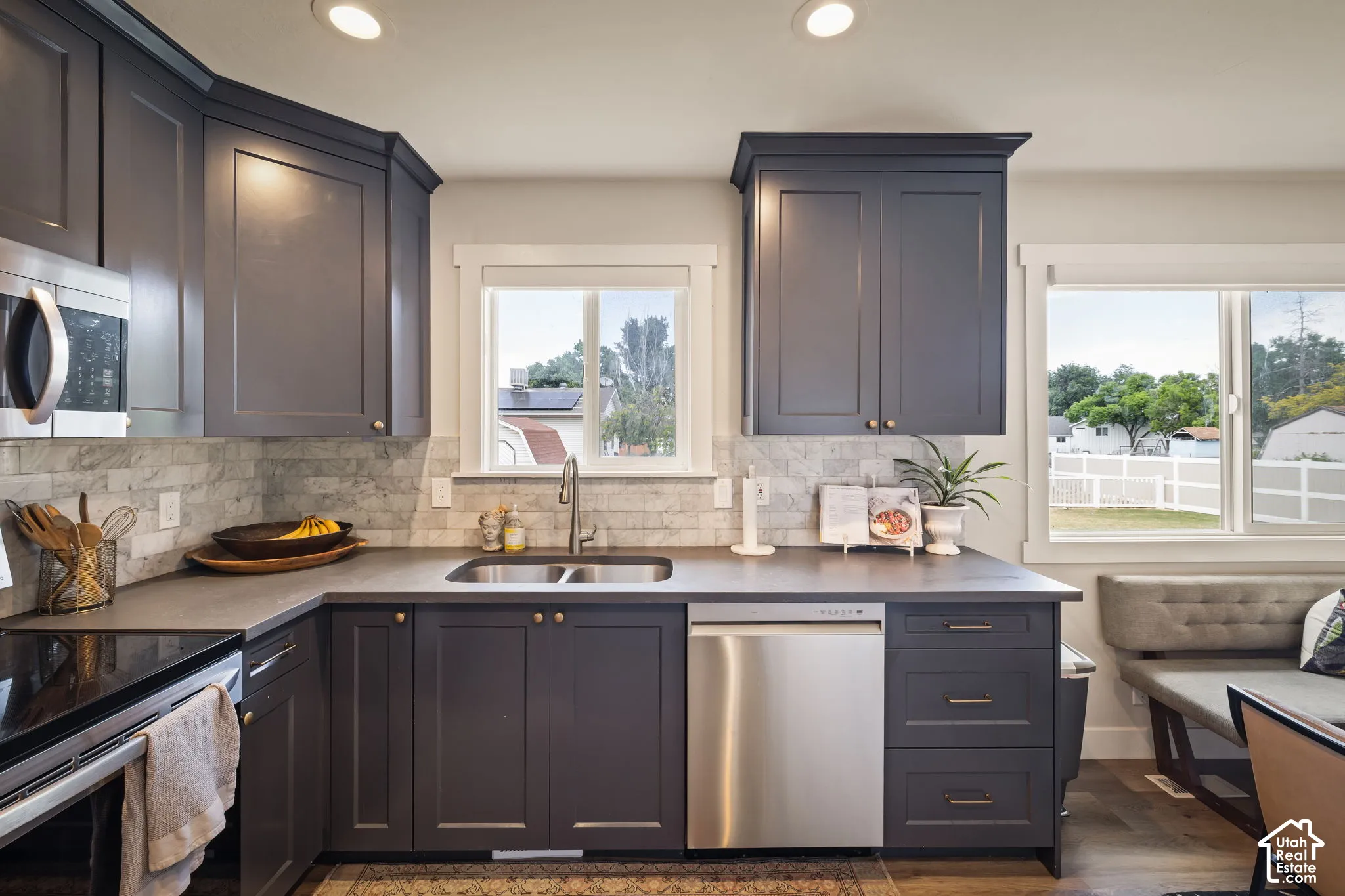 Kitchen featuring dark cabinetry, stone-finish countertops, tile backsplash, and stainless steel appliances