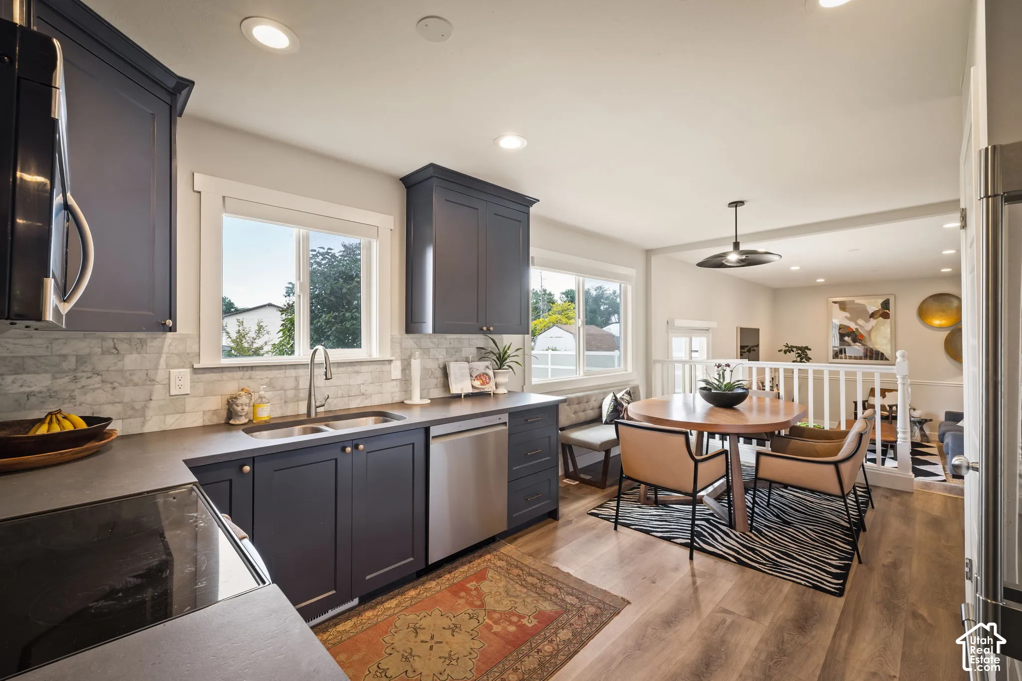 Modern kitchen featuring dark cabinetry, stainless steel appliances, a tile backsplash, and wood-finish flooring