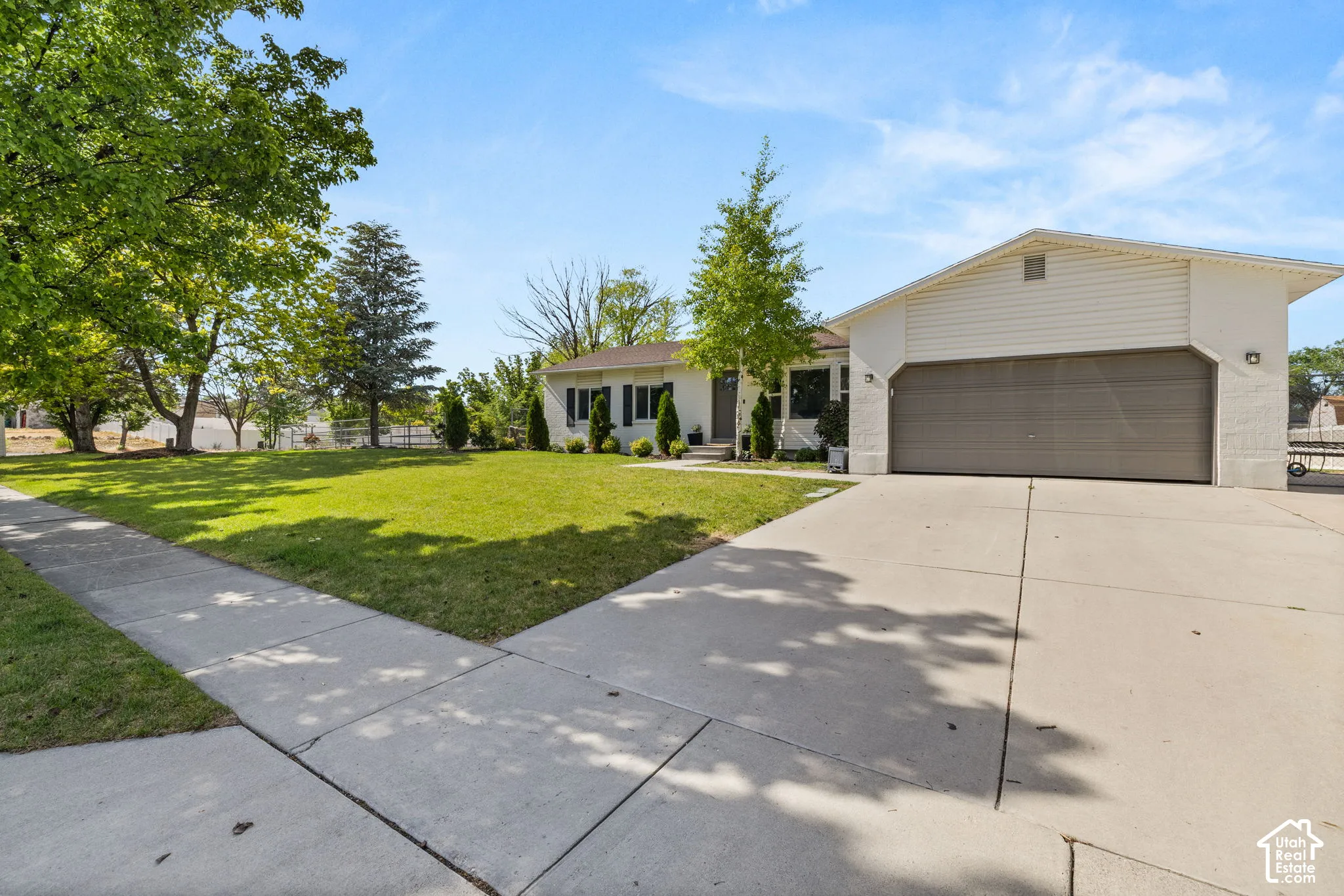 Single-story residence featuring a large front yard with mature trees, a broad concrete driveway, and an attached two-car garage