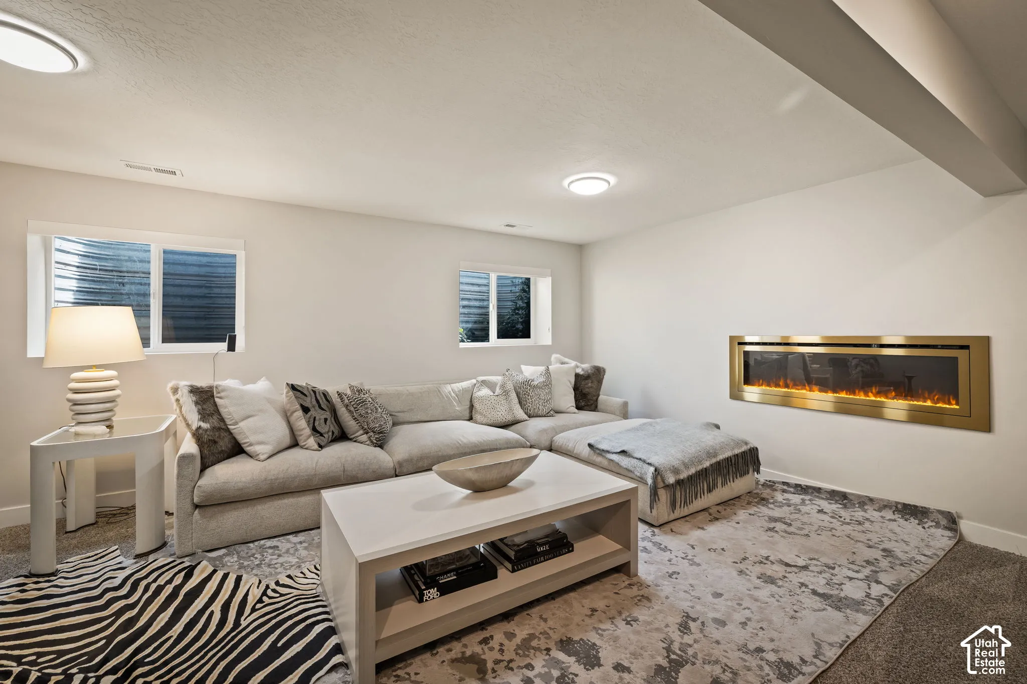 Living space with a wall-mounted electric fireplace featuring a gold-toned frame, two recessed windows, and a carpeted floor