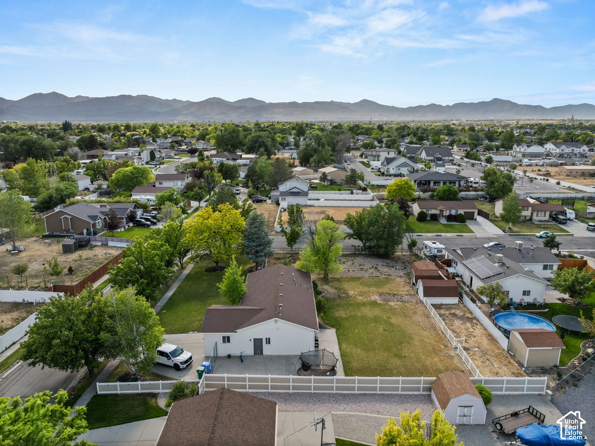 Expansive property featuring a white privacy fence, mature trees, a detached storage shed, and a mountain backdrop