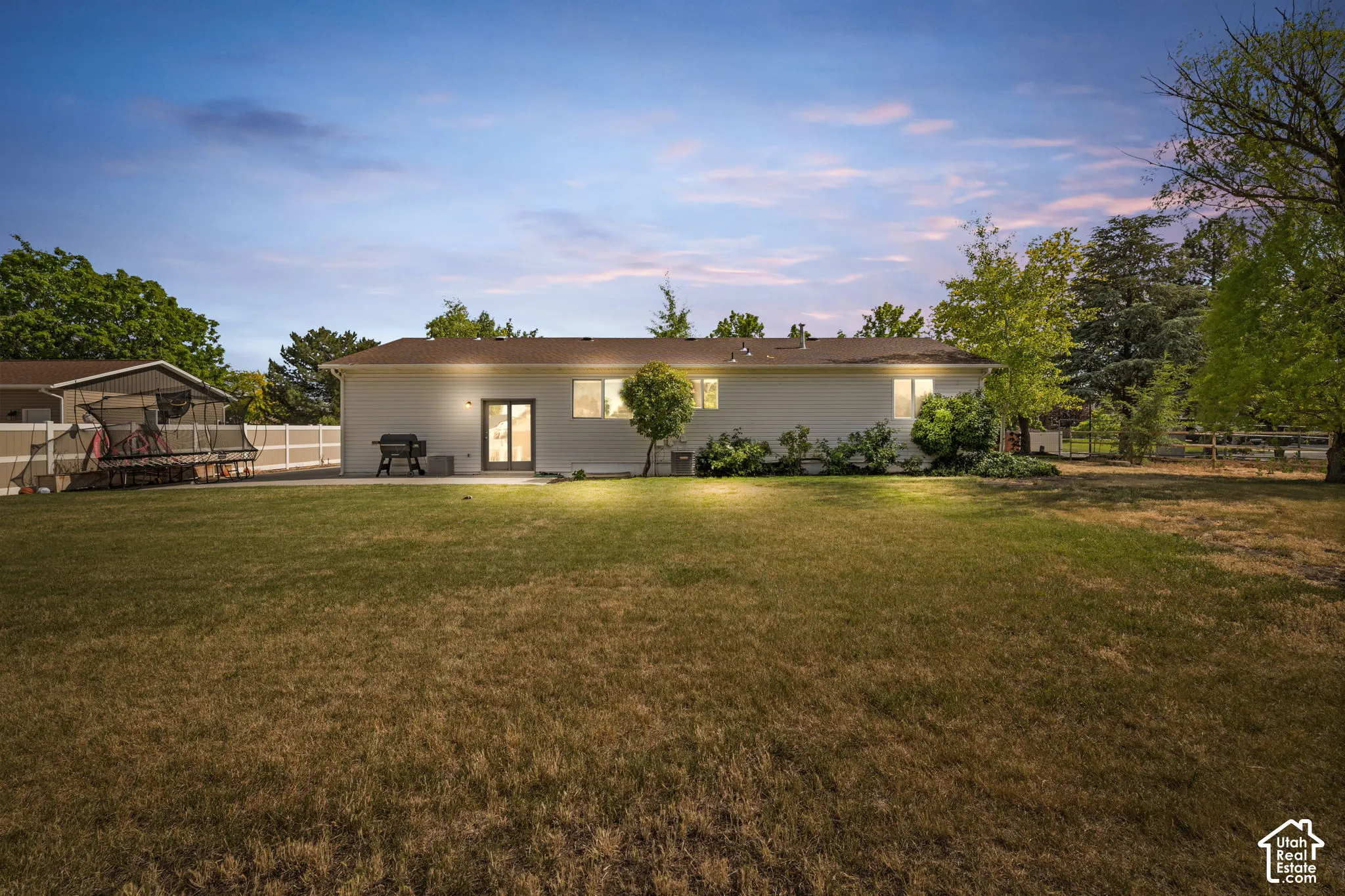 Expansive rear yard featuring a large grass area, mature trees, and a white privacy fence