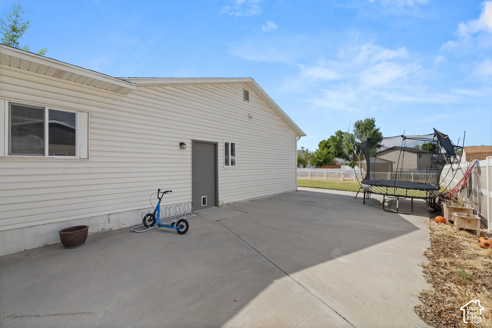 Expansive concrete patio area extending along the side of the residence, featuring vinyl siding and multiple windows