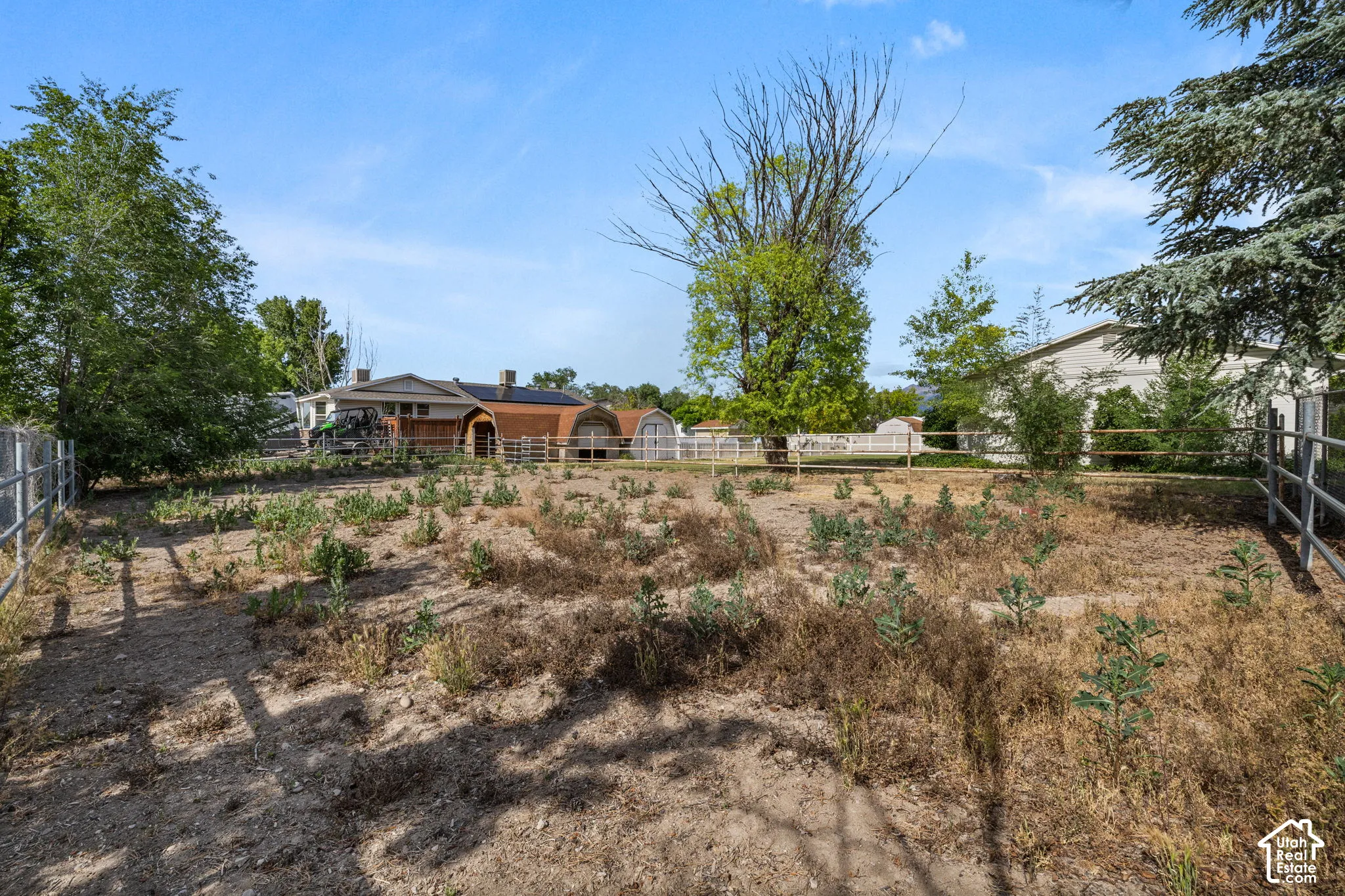 Expansive property featuring a metal rail fence, mature trees, and a wooden perimeter fence