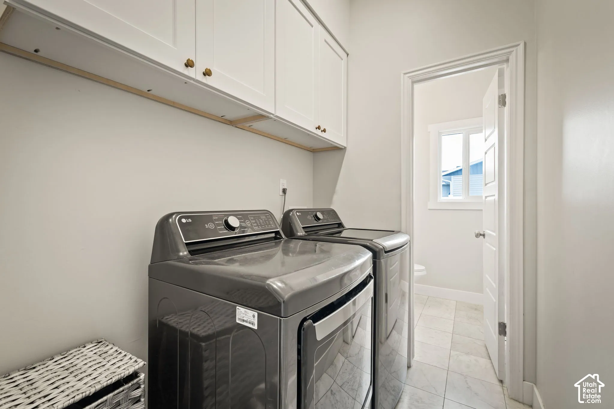 Dedicated laundry area featuring overhead white cabinetry with brass-toned hardware, light gray walls, and tile flooring