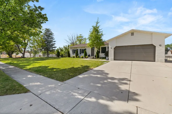 Single-story residence featuring a large front yard with mature trees, a broad concrete driveway, and an attached two-car garage