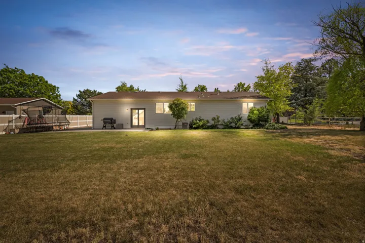 Expansive rear yard featuring a large grass area, mature trees, and a white privacy fence