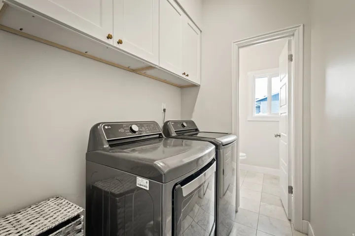 Dedicated laundry area featuring overhead white cabinetry with brass-toned hardware, light gray walls, and tile flooring
