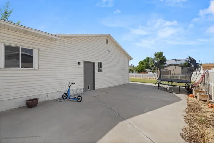 Expansive concrete patio area extending along the side of the residence, featuring vinyl siding and multiple windows