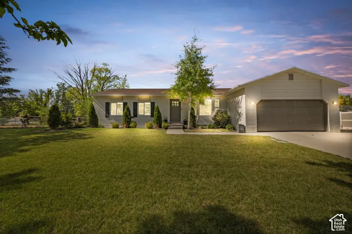 Ranch-style residence featuring a two-car garage, manicured front lawn, and mature trees