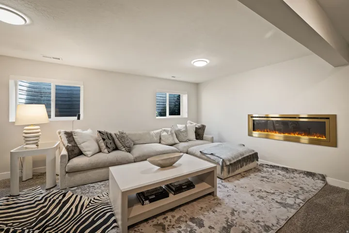 Living space with a wall-mounted electric fireplace featuring a gold-toned frame, two recessed windows, and a carpeted floor