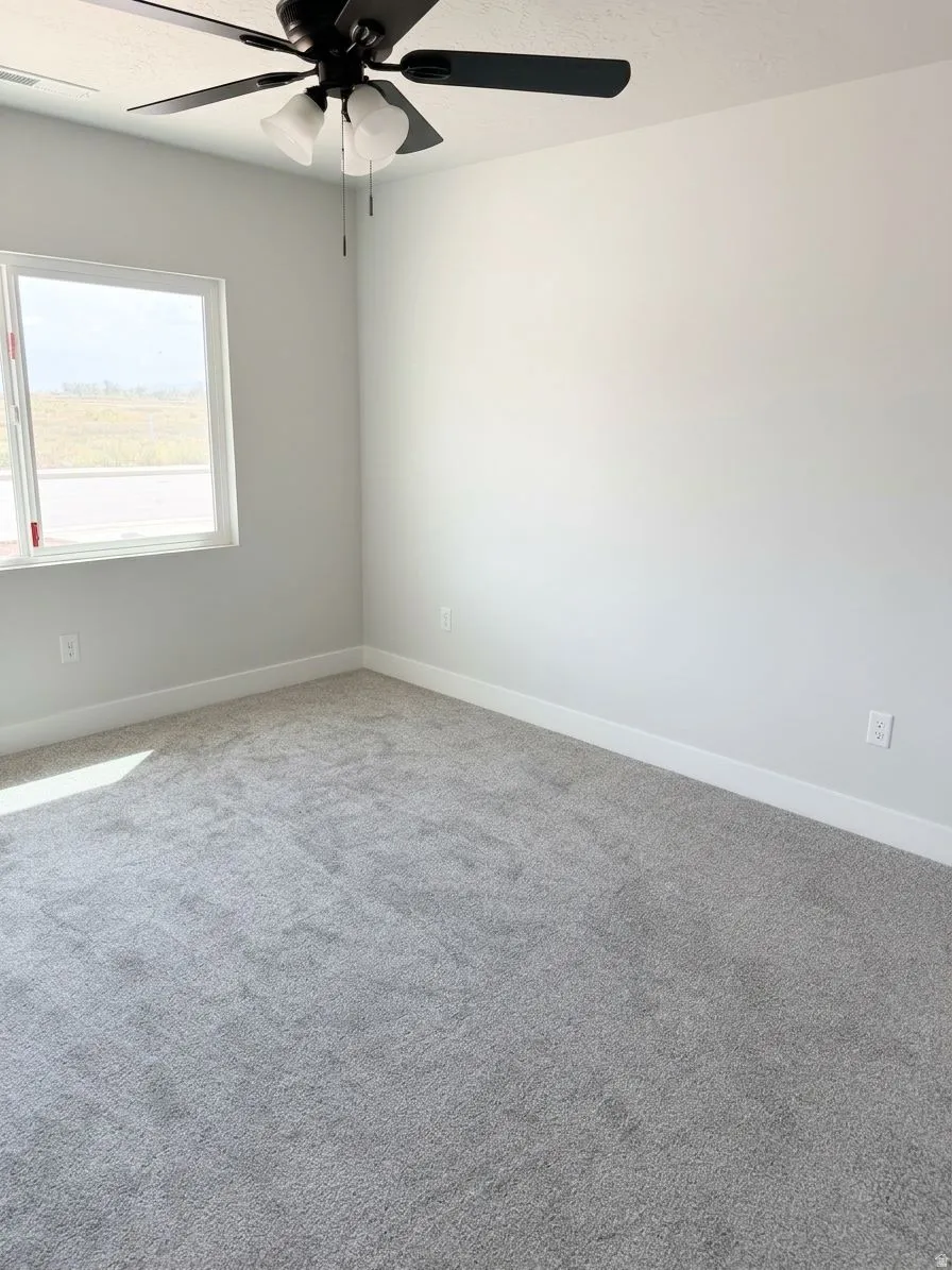 Gray wall-to-wall carpeting, white walls, and a white window frame with a black ceiling fan