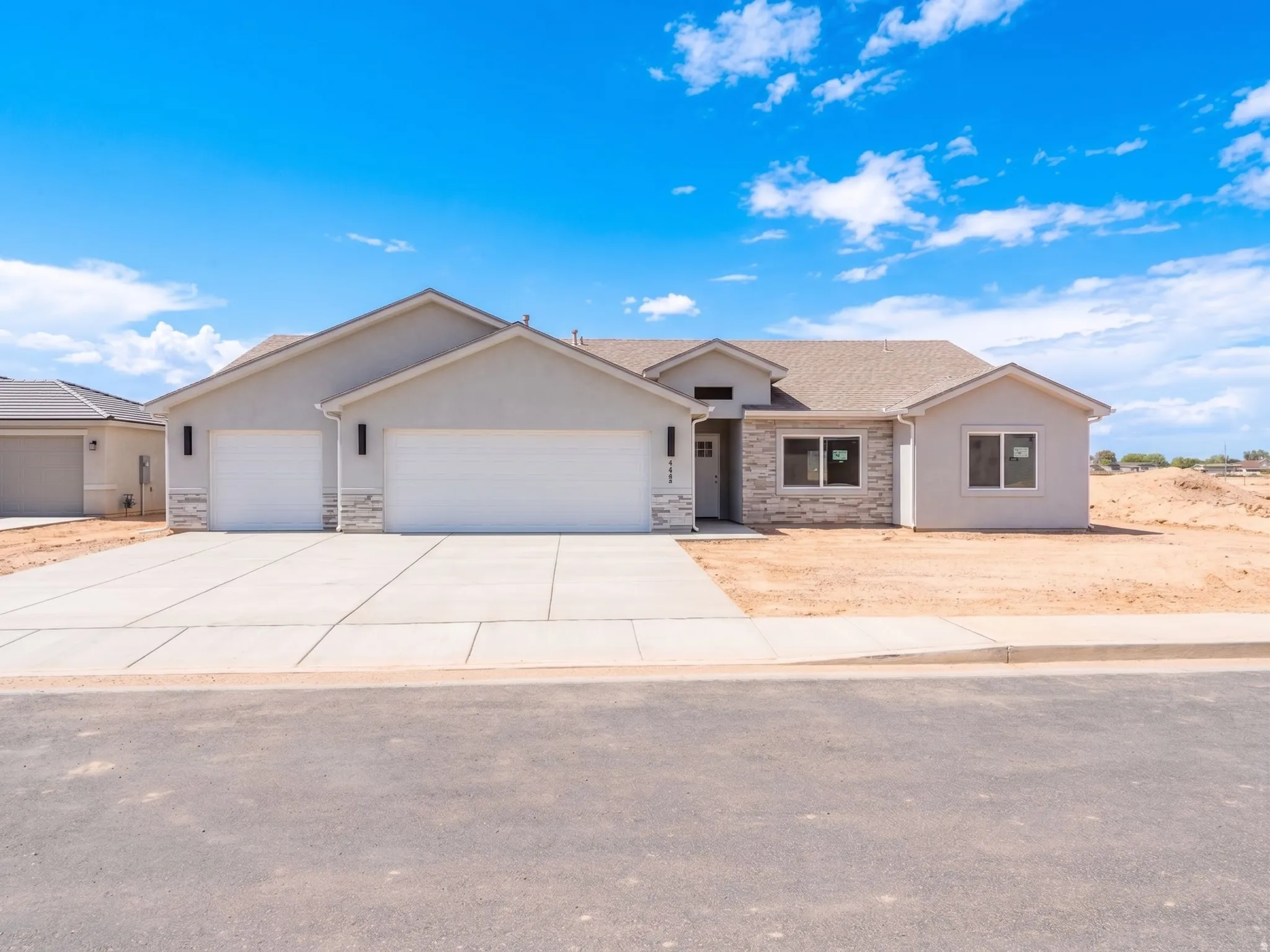 Stucco exterior with stone accents, concrete driveway, two garage doors, and a covered entry