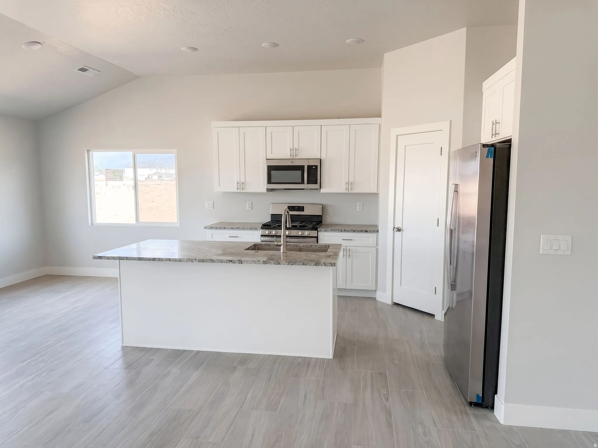 Kitchen featuring white cabinetry, stainless steel appliances, a center island with a sink, and wood-finish flooring