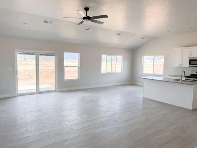Vaulted ceiling with a ceiling fan, light-toned wood-finish flooring, white kitchen cabinetry with a light-toned countertop, and multiple windows