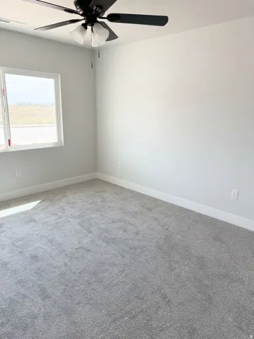 Gray wall-to-wall carpeting, white walls, and a white window frame with a black ceiling fan
