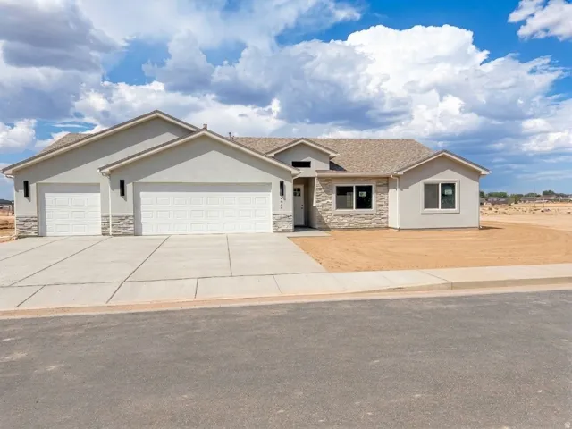 Stucco exterior with stone accent, asphalt shingle roof, attached three-car garage, concrete driveway, and concrete sidewalk