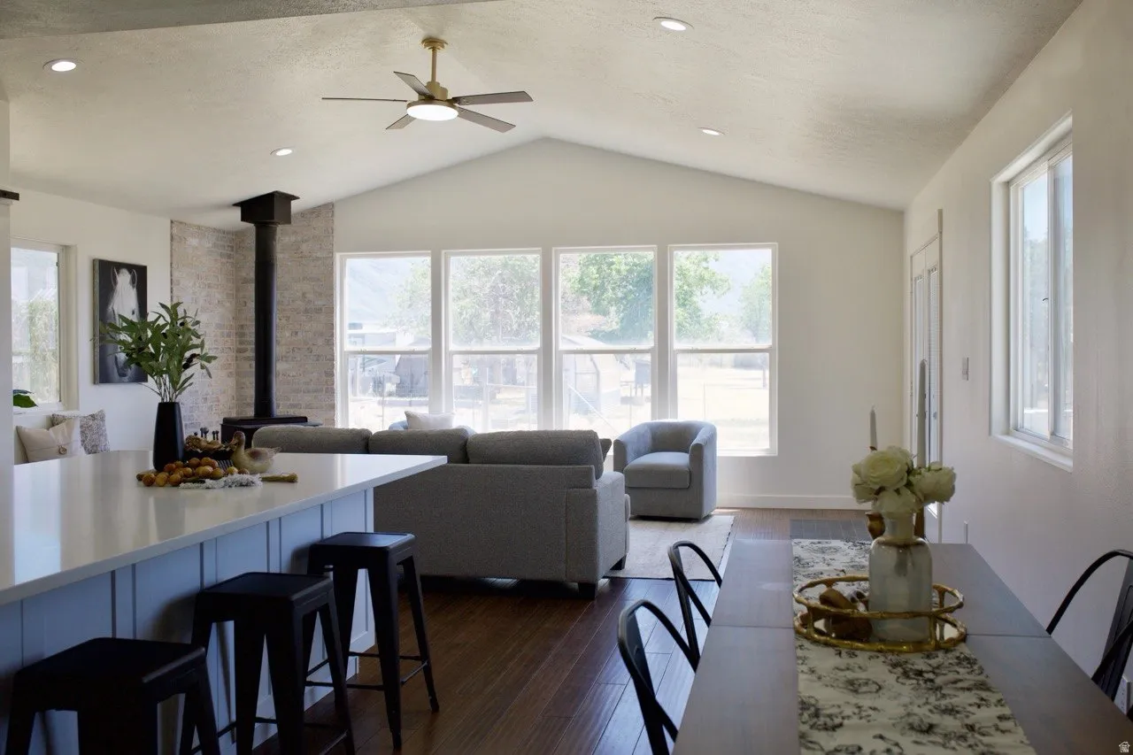 Open-concept living space featuring vaulted ceilings, a prominent brick-clad fireplace, and wood-finish flooring