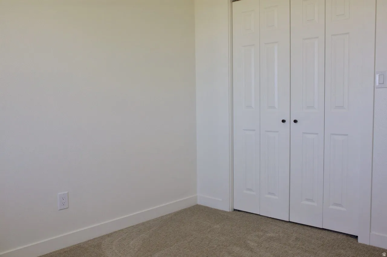 White bi-fold closet doors with black knobs complement the neutral wall finishes and plush carpeting