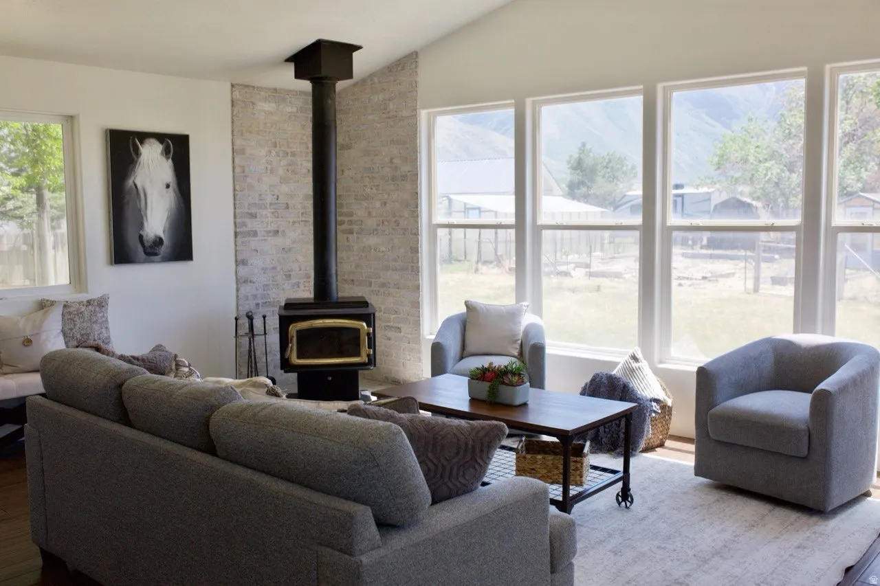 Living area featuring a wood-burning stove with a brick-finish accent wall, vaulted ceilings, and large windows with outdoor scenery