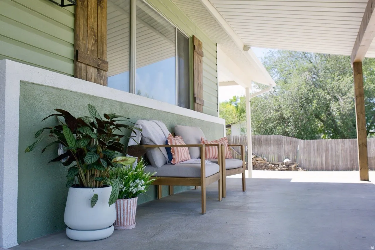 Covered concrete patio with a painted stucco half-wall, vinyl siding, and rustic wood shutters