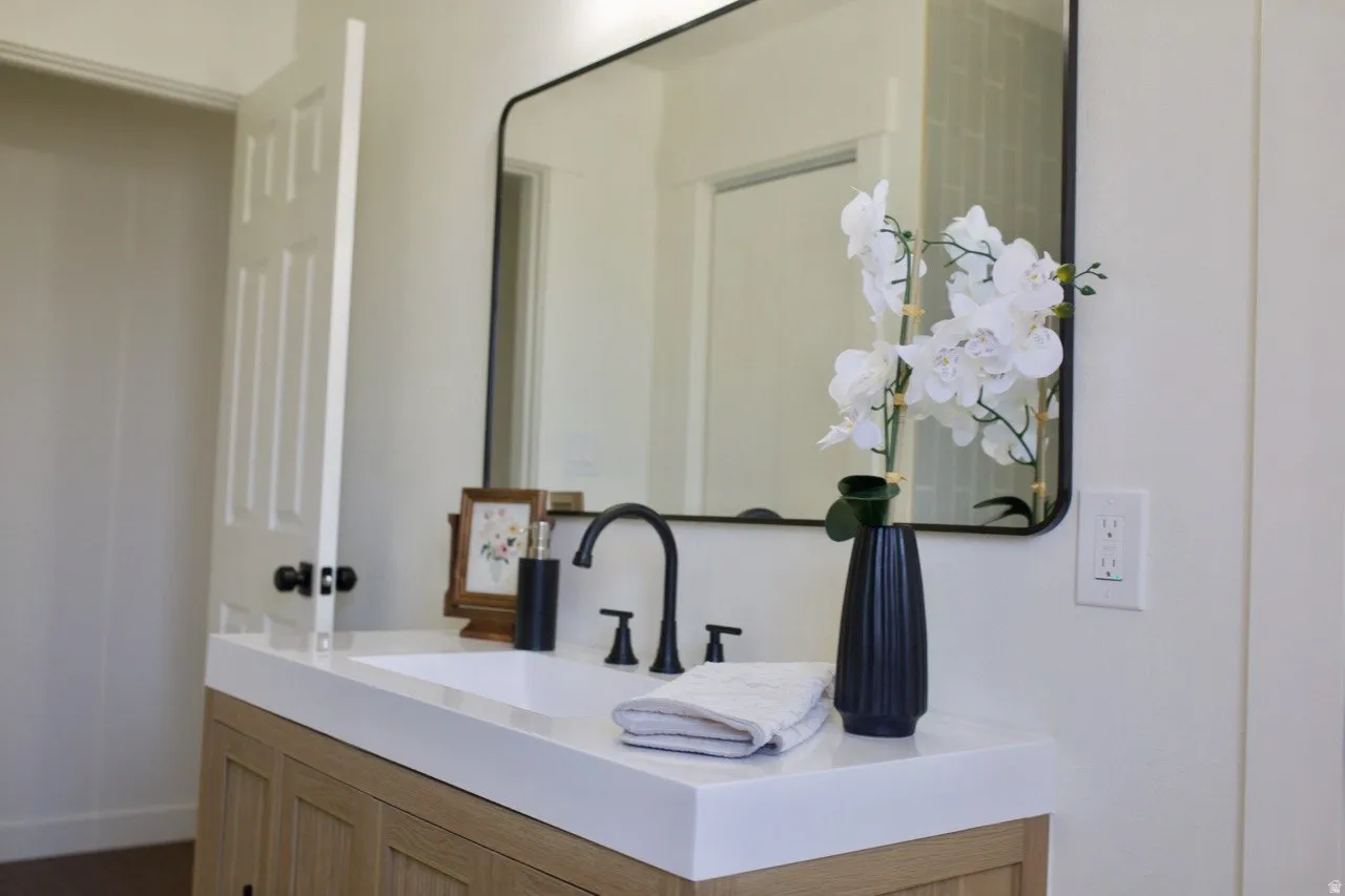 Modern bathroom vanity featuring a light wood-finish cabinet, a white countertop with an integrated rectangular sink, and a black arch-framed mirror