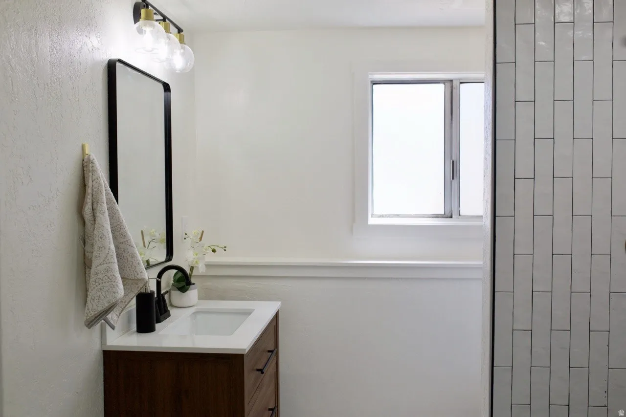 Bathroom vanity featuring a wood-finish cabinet with black hardware, white countertop, and integrated sink