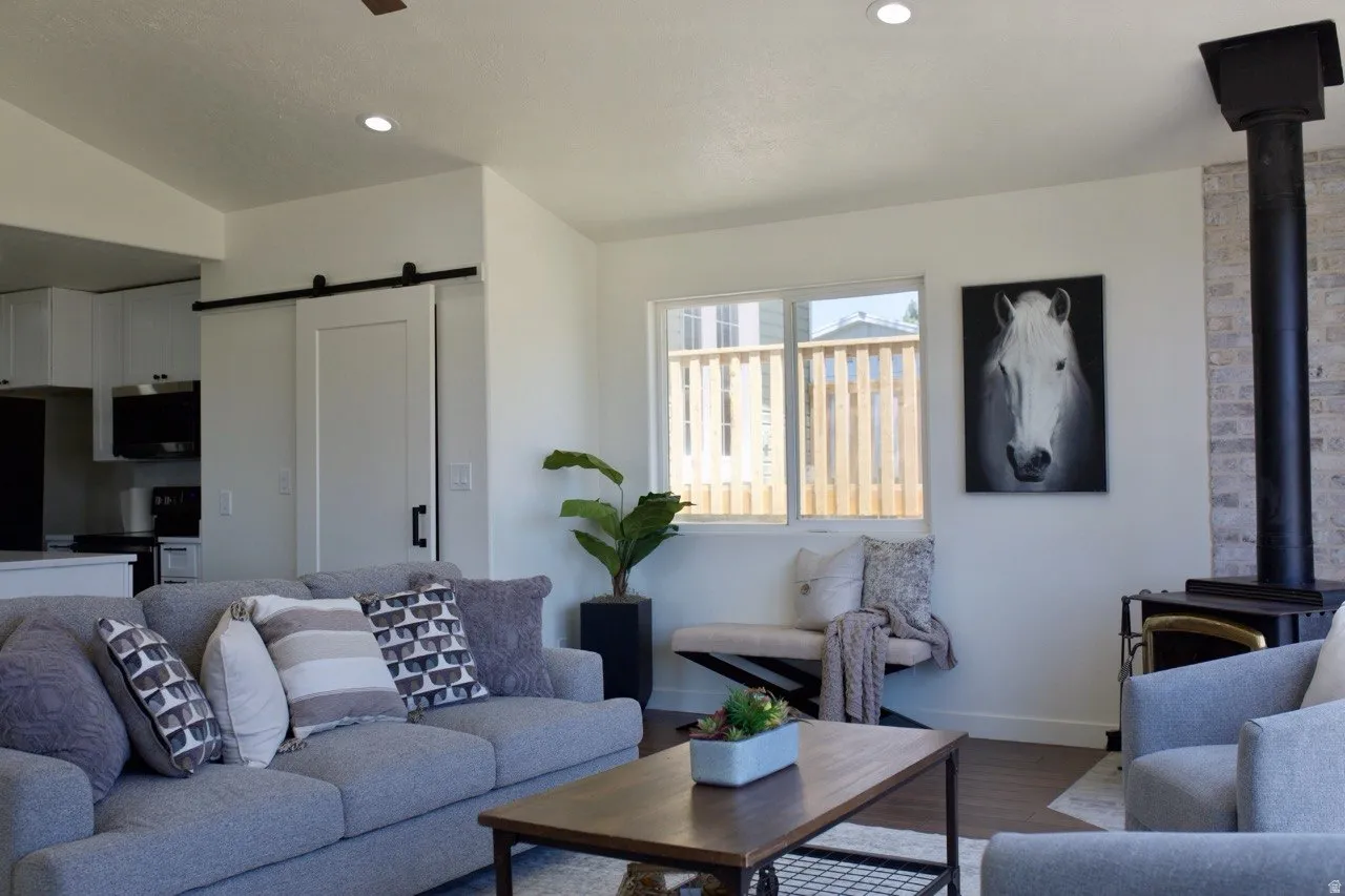 Living space featuring recessed lighting, wood-finish flooring, a wood-burning stove with a brick-finish surround, and a sliding barn door