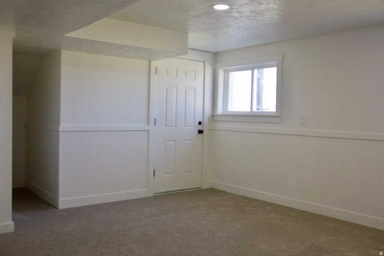 Carpeted room featuring white walls with wainscoting, a paneled interior door, and a single window with white trim