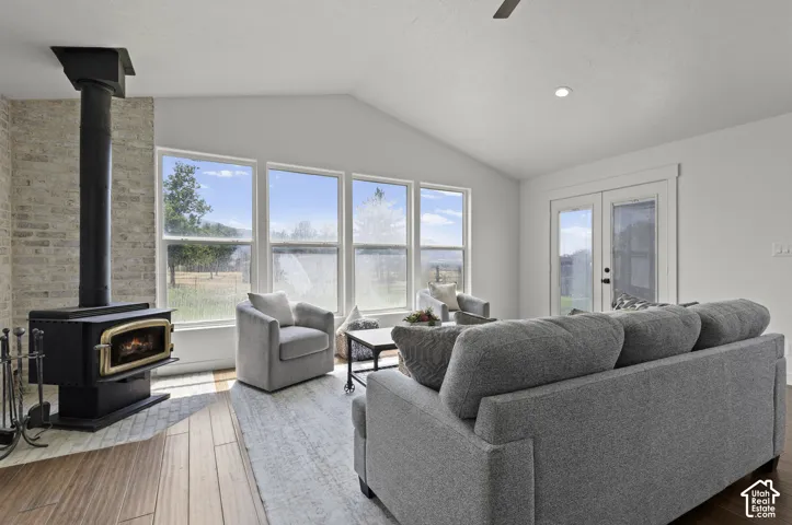 Vaulted ceiling with recessed lighting, wood-burning stove with brick surround, wood-finish flooring, large windows, and double glass-paneled doors