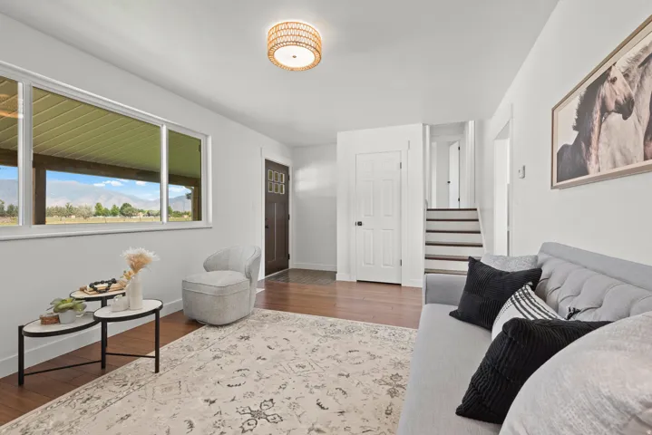 Hardwood flooring, white painted walls, large window with outdoor scenery, recessed stairway, and a decorative ceiling light fixture