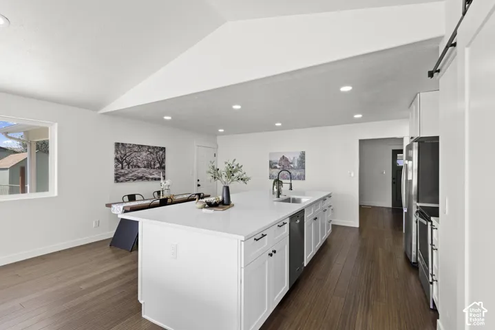 Open-concept kitchen with a large island, white shaker cabinetry, stainless steel appliances, and wood-finish flooring