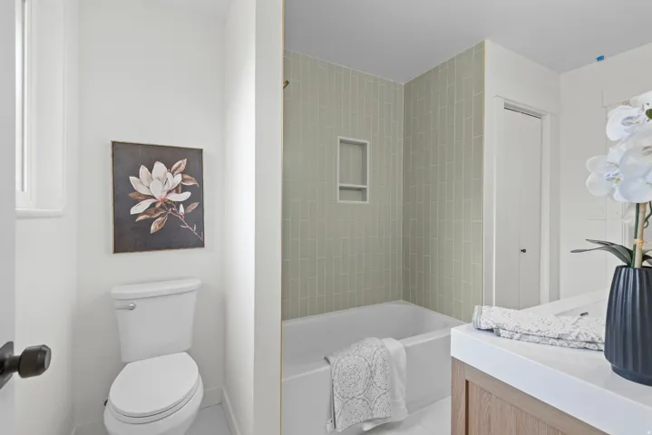 Bathtub with subway tile surround, integrated shower niche, and a light wood-finish vanity with a white countertop