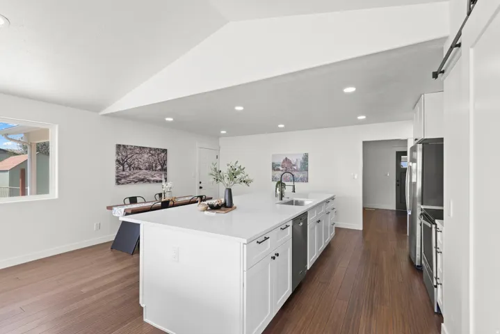 Open-concept kitchen with a large island, white shaker cabinetry, stainless steel appliances, and wood-finish flooring